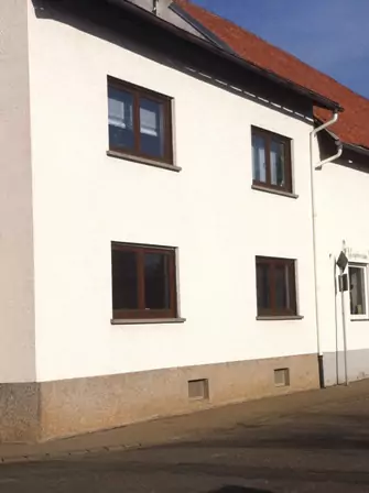 Schlichte weiße Außenwand eines Wohnhauses nach Fassadensanierung mit braunen Fensterrahmen.