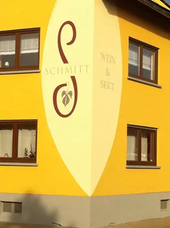 Großes Wandlogo „Schmitt Wein & Sekt“ auf einer gelben Hausfassade mit dekorativem Schriftzug.