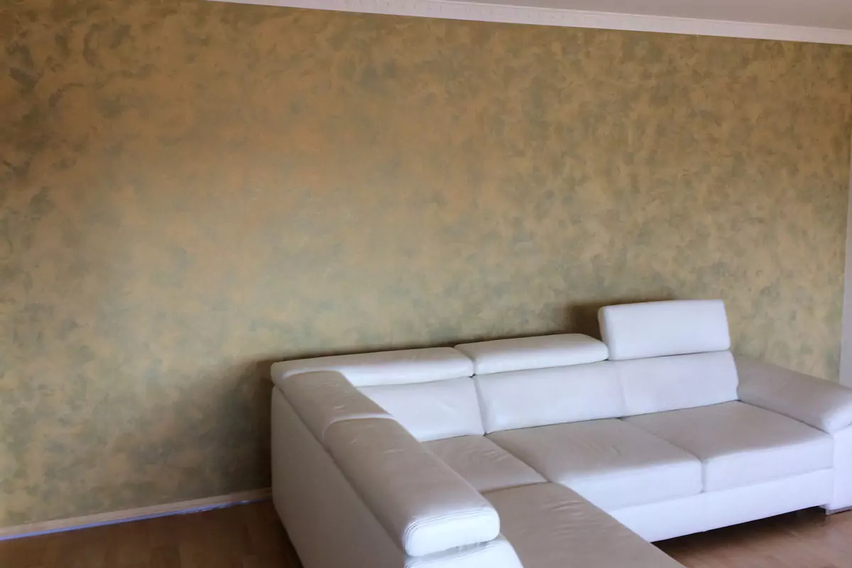 Wohnzimmerwand in Wischtechnik mit Beige-Grün-Effekt hinter weißem Ledersofa.