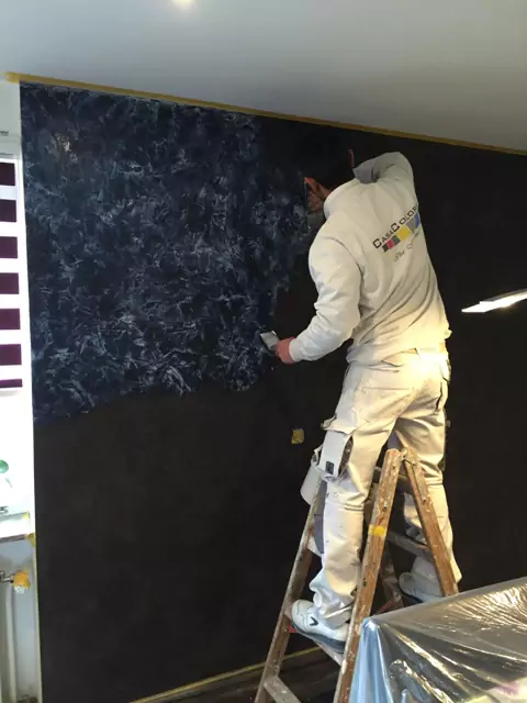 Handwerker trägt blaue Spachteltechnik auf schwarze Wand für individuelle Optik auf.