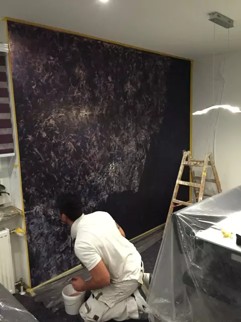 Maler bringt Effektfarbe in dunklen Tönen auf vorbereitete Wand im Wohnraum auf.