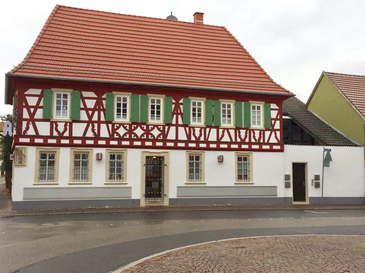 Renoviertes Fachwerkhaus mit roten Balken, weißer Fassade und grünen Fensterläden nach Sanierung.