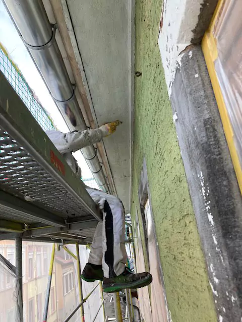 Maler auf Gerüst führt Arbeiten an der grünen Fassade eines Altbaus durch.