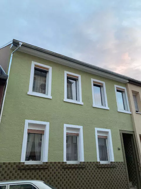 Blick auf die frisch sanierte grüne Hauswand mit frisch gestrichenen weißen Fensterrahmen