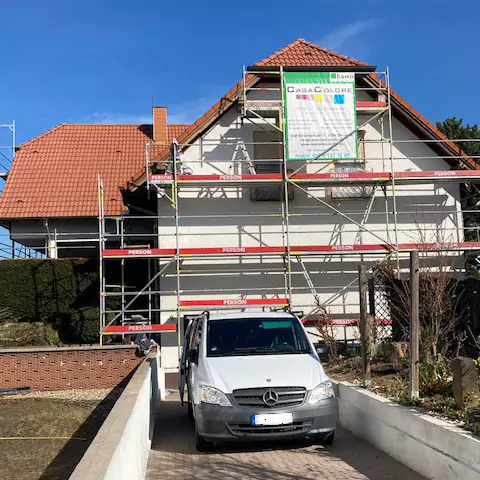 Blick auf eine Einfahrt mit einem Haus und einem Baugerüst davor im Hintergrund.