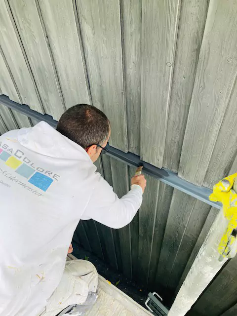 Malermeister auf einem Baugerüst beim Streichen einer Holzwand mit Holzschutzmittel