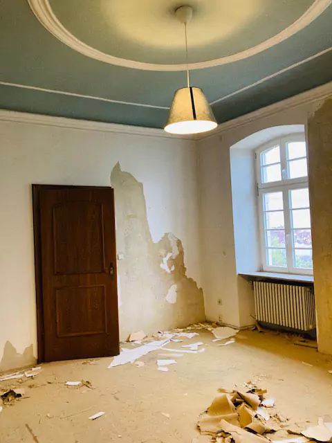 Blick in einen Raum im Altbau während der Renovierung mit abgeblätterter Farbe und Tapete