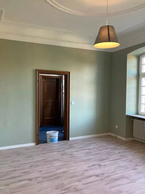 Blick in einen grün gestrichenen Raum mit Deckenlampe und Farbeimer im Türrahmen